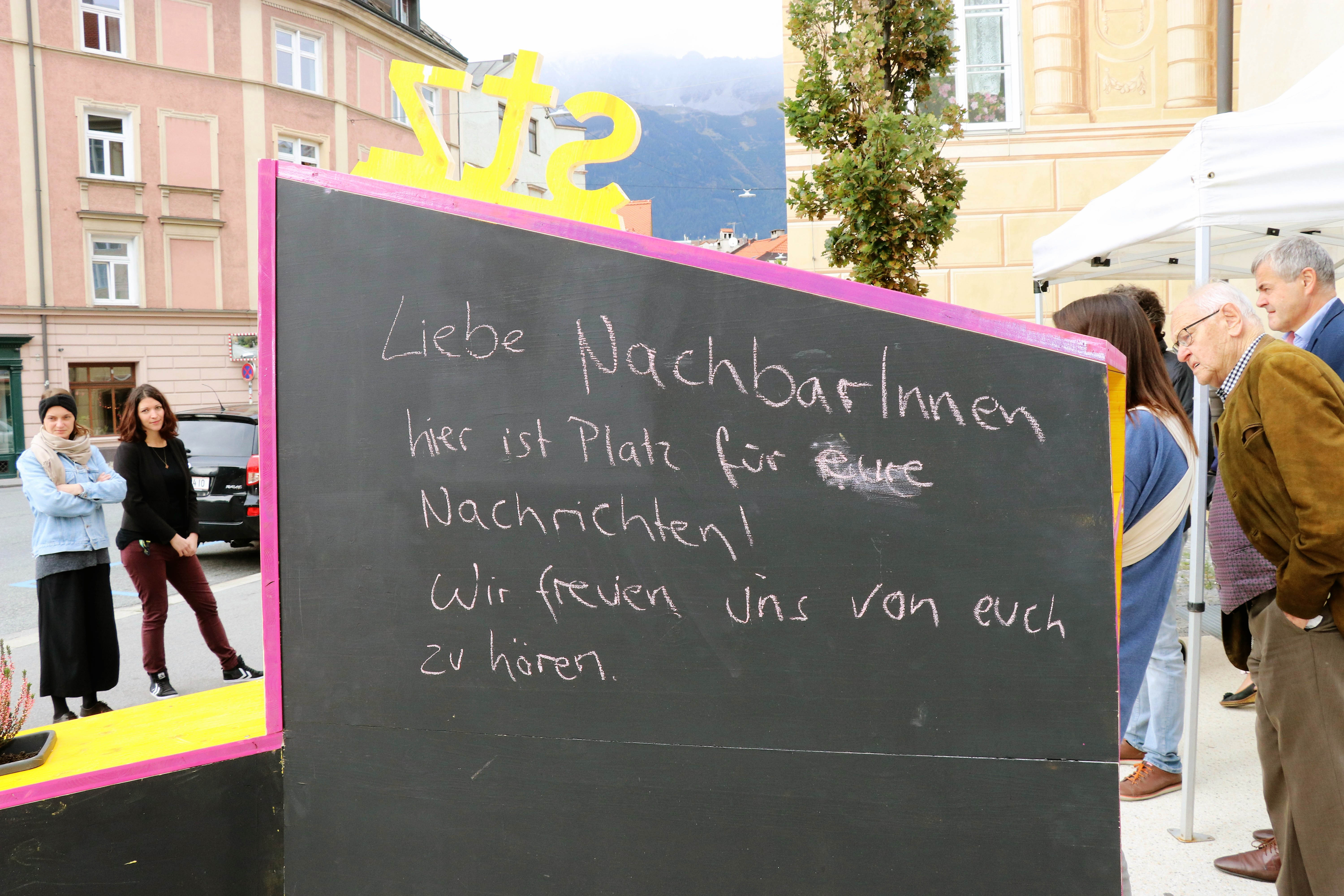 Kreativ, bunt und unübersehbar – so präsentiert sich seit 4. Oktober das temporäre, öffentliche Möbelstück vor dem Stadtteilzentrum Wilten in der Leopoldstraße 33a. Die Idee für das hölzerne Bauwerk entstand im Rahmen eines Beteiligungsprozesses bereits im Dezember 2017. Damals kamen NachbarInnen, ein Kreativteam aus Wilten und VertreterInnen des Stadtteilzentrums zusammen, um über die Gestaltung des Innenhofes zu beratschlagen. Die nun realisierte Konstruktion enthält die gewünschten Elemente, bestehend aus Beschriftung, Informations- und Plakatflächen, einem Buchtauschregal, Sitzgelegenheiten und kann mit Blumentöpfen ausgestattet werden. Bei der Einweihung kamen viele Beteiligte und UnterstützerInnen zusammen, unter ihnen auch Gemeinderätin Janine Bex, Geschäftsführer Hubert Innerebner (Innsbrucker Sozialen Dienste, ISD), Stadtteilkoordinatorin Florence Fritz sowie das Kreativteam rund um Charly Walter und zahlreiche AnrainerInnen. Bis Juni 2021 lädt das öffentliche Möbelstück vor dem Stadtteilzentrum Wilten zum Verweilen und Verwenden ein. AA