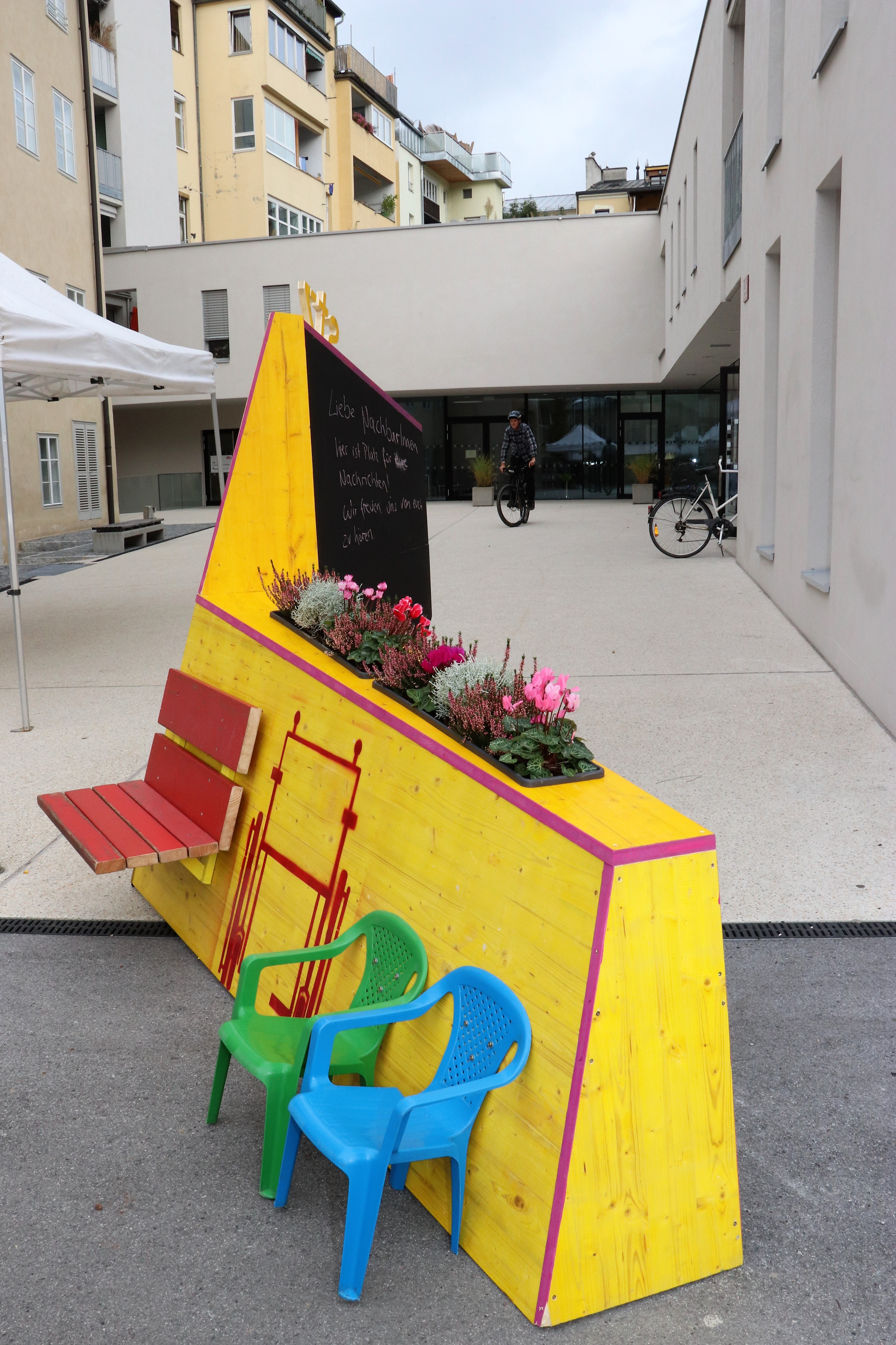 Kreativ, bunt und unübersehbar – so präsentiert sich seit 4. Oktober das temporäre, öffentliche Möbelstück vor dem Stadtteilzentrum Wilten in der Leopoldstraße 33a. Die Idee für das hölzerne Bauwerk entstand im Rahmen eines Beteiligungsprozesses bereits im Dezember 2017. Damals kamen NachbarInnen, ein Kreativteam aus Wilten und VertreterInnen des Stadtteilzentrums zusammen, um über die Gestaltung des Innenhofes zu beratschlagen. Die nun realisierte Konstruktion enthält die gewünschten Elemente, bestehend aus Beschriftung, Informations- und Plakatflächen, einem Buchtauschregal, Sitzgelegenheiten und kann mit Blumentöpfen ausgestattet werden. Bei der Einweihung kamen viele Beteiligte und UnterstützerInnen zusammen, unter ihnen auch Gemeinderätin Janine Bex, Geschäftsführer Hubert Innerebner (Innsbrucker Sozialen Dienste, ISD), Stadtteilkoordinatorin Florence Fritz sowie das Kreativteam rund um Charly Walter und zahlreiche AnrainerInnen. Bis Juni 2021 lädt das öffentliche Möbelstück vor dem Stadtteilzentrum Wilten zum Verweilen und Verwenden ein. AA