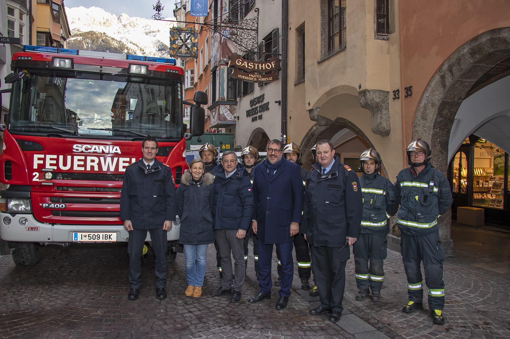 Vizebürgermeister Franz X. Gruber (Bildmitte), gemeinsam mit  Branddirektor Helmut Hager (l.), Branddirektor-Stellvertreter Johann Zimmermann (3. v. r.), den Hotelbesitzern Brigitte Tschoner (2. v. l.) und Thomas Hudovernik (4. v. l.) sowie eine Mannschaft der Berufsfeuerwehr vor dem altehrwürdigen Hotel Weißes Kreuz in der Altstadt.