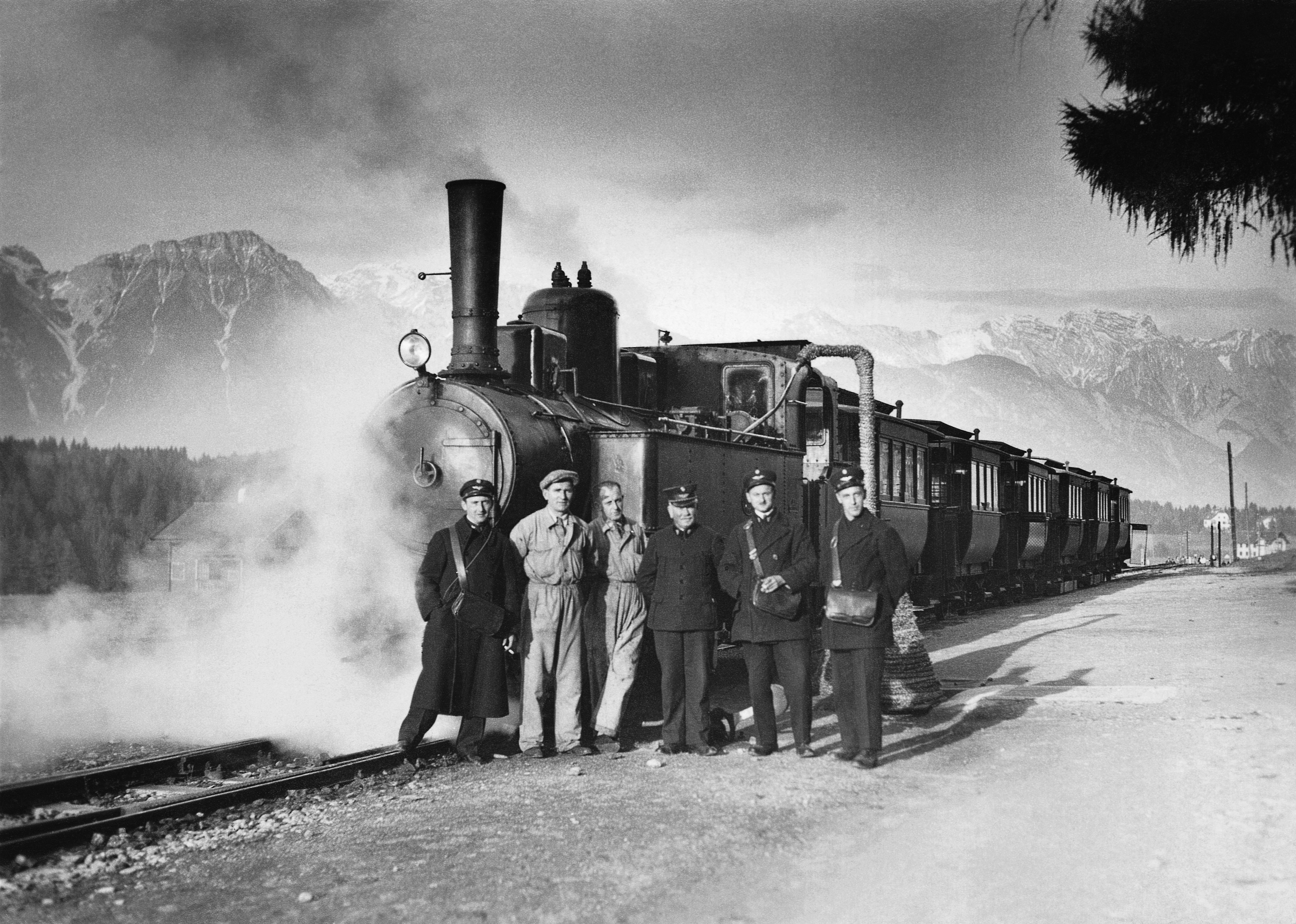 Die Innsbrucker Mittelgebirgsbahn, die „Igler“, mit sechs Waggons in der Station Igls, 1932. Stolz posiert das  Straßenbahnpersonal mit Lokomotivführer, Heizer und Schaffner vor der bis 1936 mit Dampf betriebenen Garnitur.