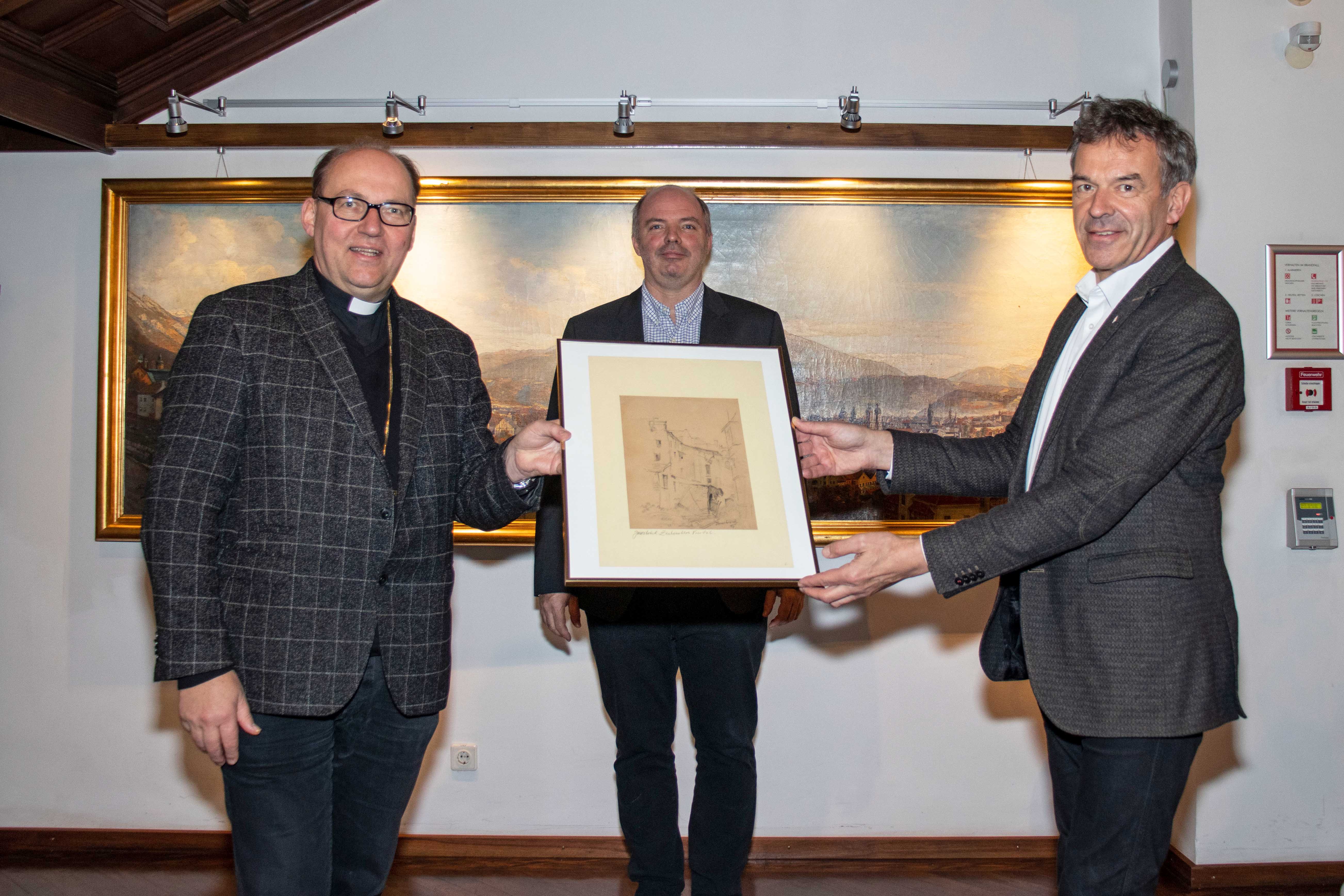 Ein besonderes Geschenk erhielt Bürgermeister Georg Willi (r.) von Bischof Hermann Glettler (l.): Eine Zeichnung des Innsbrucker Künstlers Wilhelm Nicolaus Prachensky (1898-1956). Der Bürgermeister gab das Werk an das Stadtarchiv/Stadtmuseum Innsbruck unter der Leitung von Lukas Morscher (M.) weiter. Es zeigt die Zerstörung der Innsbrucker Altstadt durch den Zweiten Weltkrieg. Während der Dom zu St. Jakob schwer getroffen wurde, blieb der Großteil der Wahrzeichen wie das Goldene Dachl, der Stadtturm, die Hofburg, das Helblinghaus oder die Ottoburg weitgehend von Bombenschäden verschont.