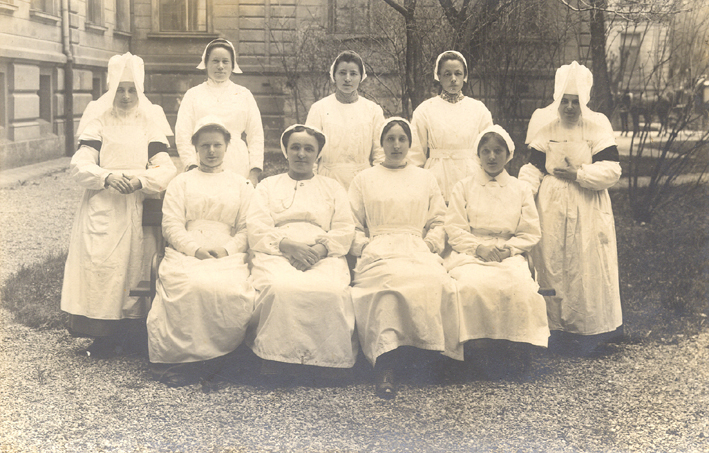 Pflegerinnenkurs im Krankenhaus Innsbruck 1917. Zu sehen sind sieben Krankenpflege-Schülerinnen und zwei Schwestern in Nonnentracht. Aufgenommen im Garten vor einem Pavillon der Klinik.