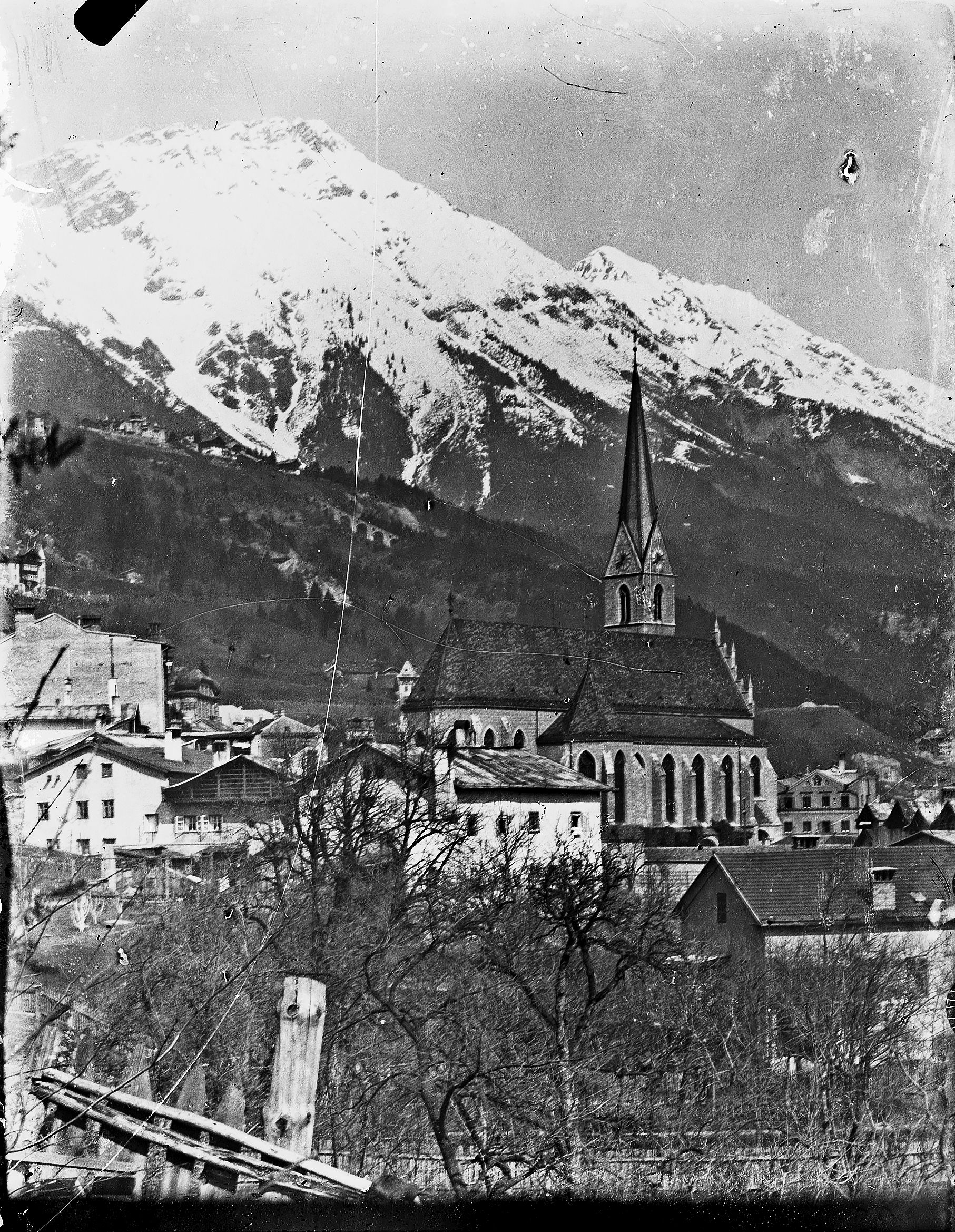 Blick auf die Pfarrkirche von St. Nikolaus und einige Wohnhäuser. Im Hintergrund kann man das Viadukt der Hungerburgbahn und die schneebedeckte Nordkette erkennen.