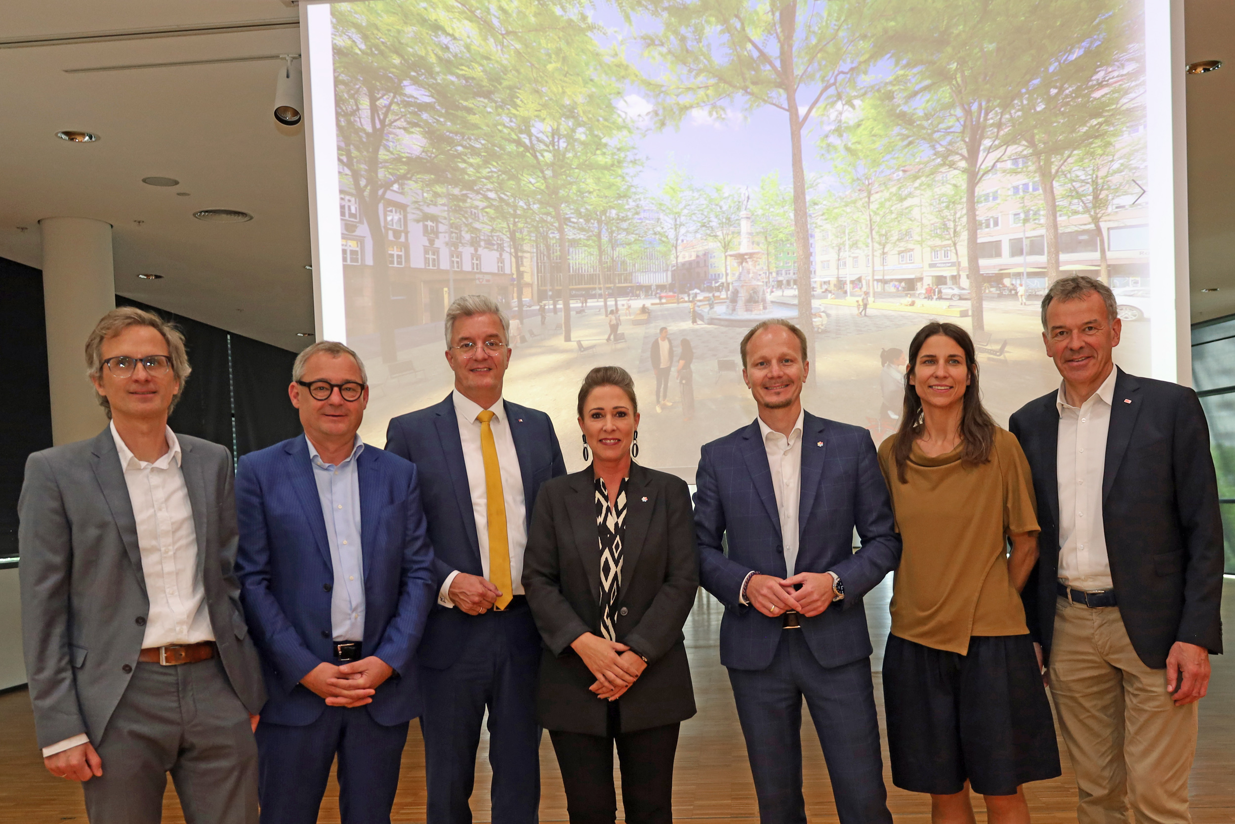 Bozner Platz wird zur Piazza: Bürgermeister Johannes Anzengruber, Vizebürgermeister Georg Willi, Stadträtin Mariella Lutz und Stadträtin Janine Bex freuen sich gemeinsam mit dem Architekten Clemens Kolar und den Vertretern des Zentrumsvereins Michael Perger und Thomas Hudovernik über den neuen Anlauf bei der Platzgestaltung.