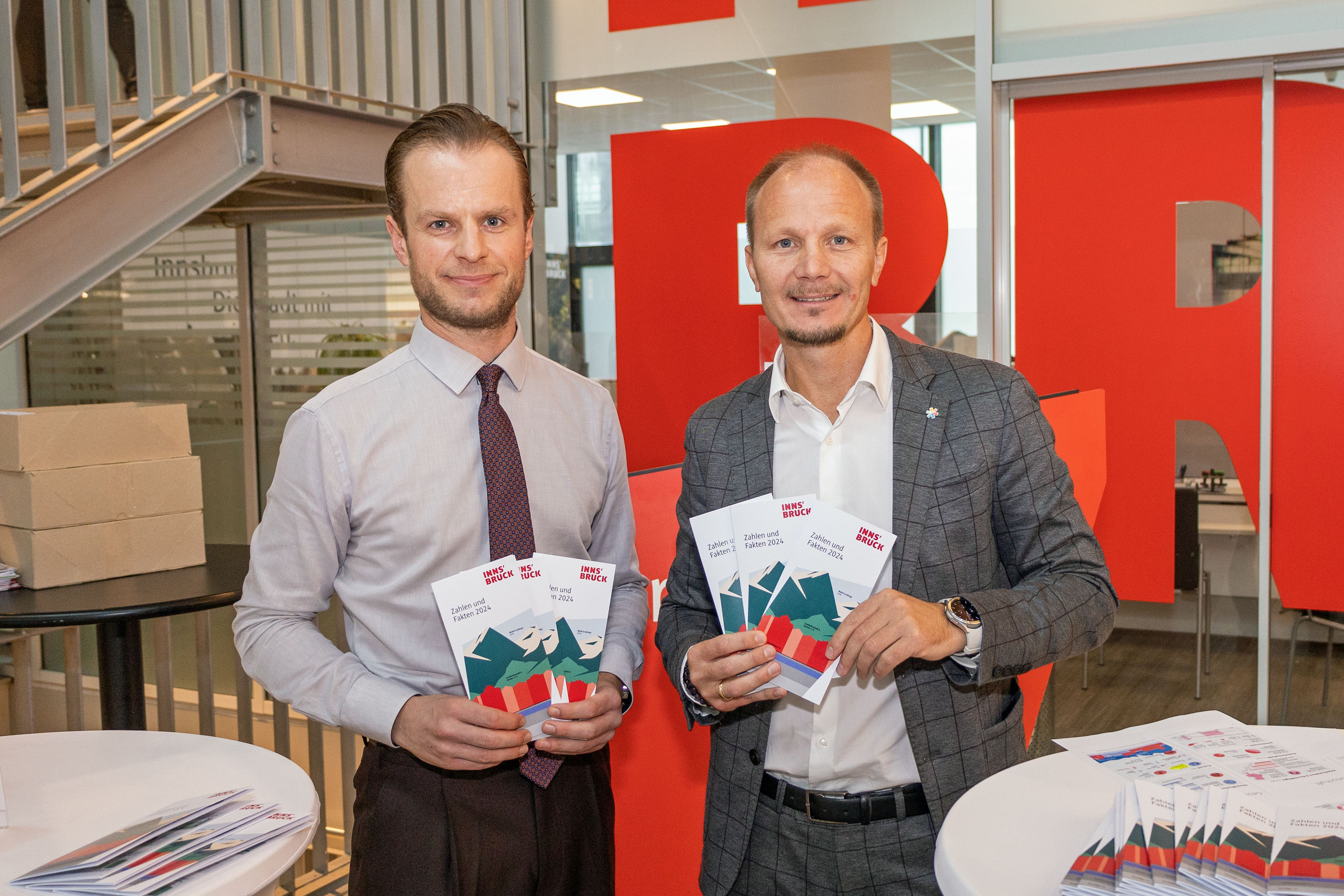 Bürgermeister Johannes Anzengruber (r.) und Amtsvorstand Mathias Behmann (l.) präsentieren die neue Statistikbroschüre der Stadt Innsbruck vor dem Bürgerservice, wo sie ab sofort erhältlich ist.