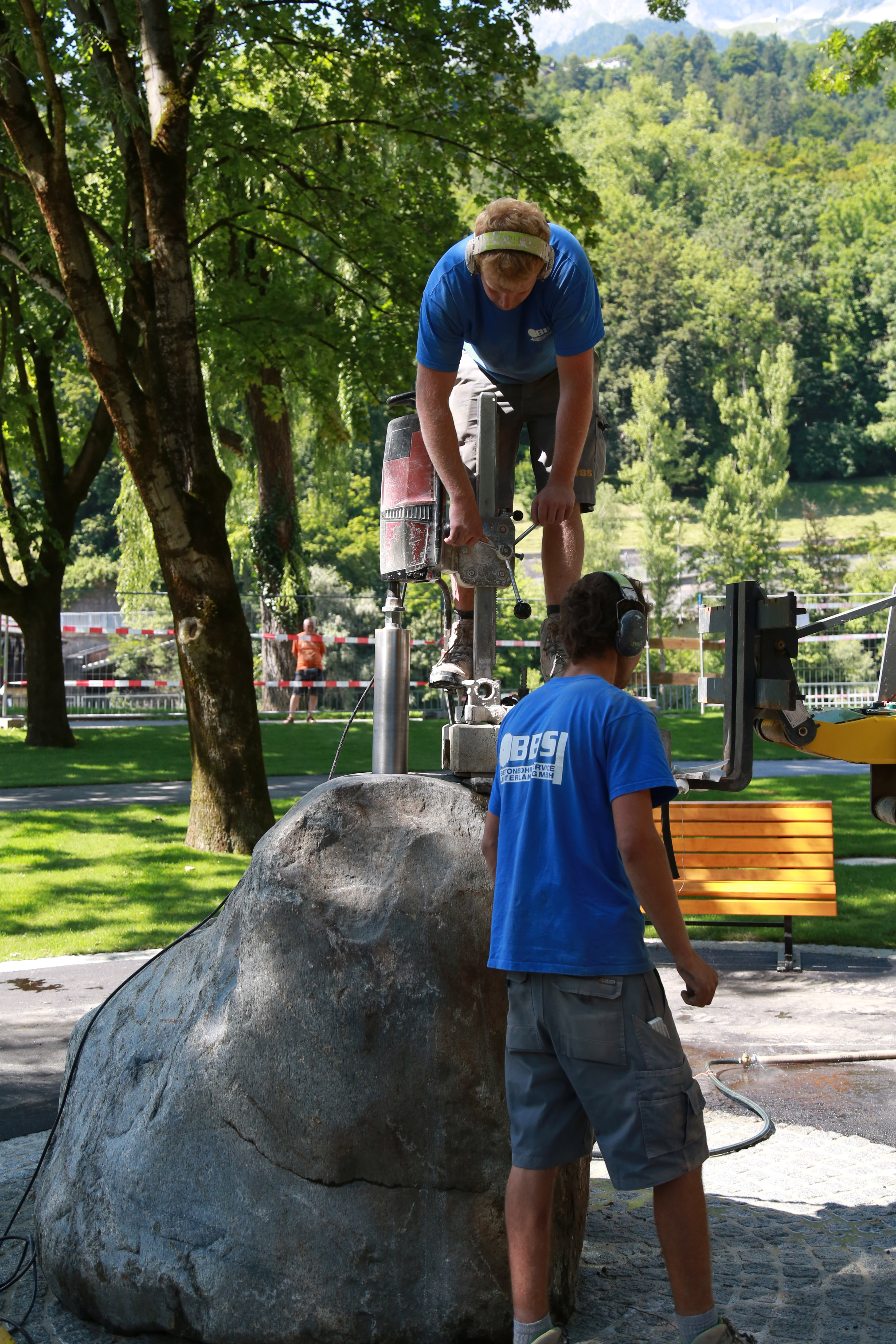 Hier wird gerade der Steinbrunnen installiert. Um diesen herum wurden gemütliche und schattige Sitzgelegenheiten errichtet, die zum Verweilen und Entspannen einladen.
